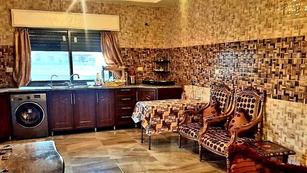 A compact kitchen with a washing machine, a dining table, and two patterned chairs. - Private Family Apartment - Very Quiet Location (Amman)