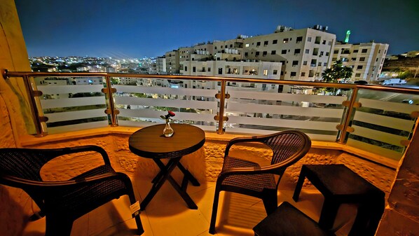 A balcony with a table and chairs, overlooking a cityscape at night.