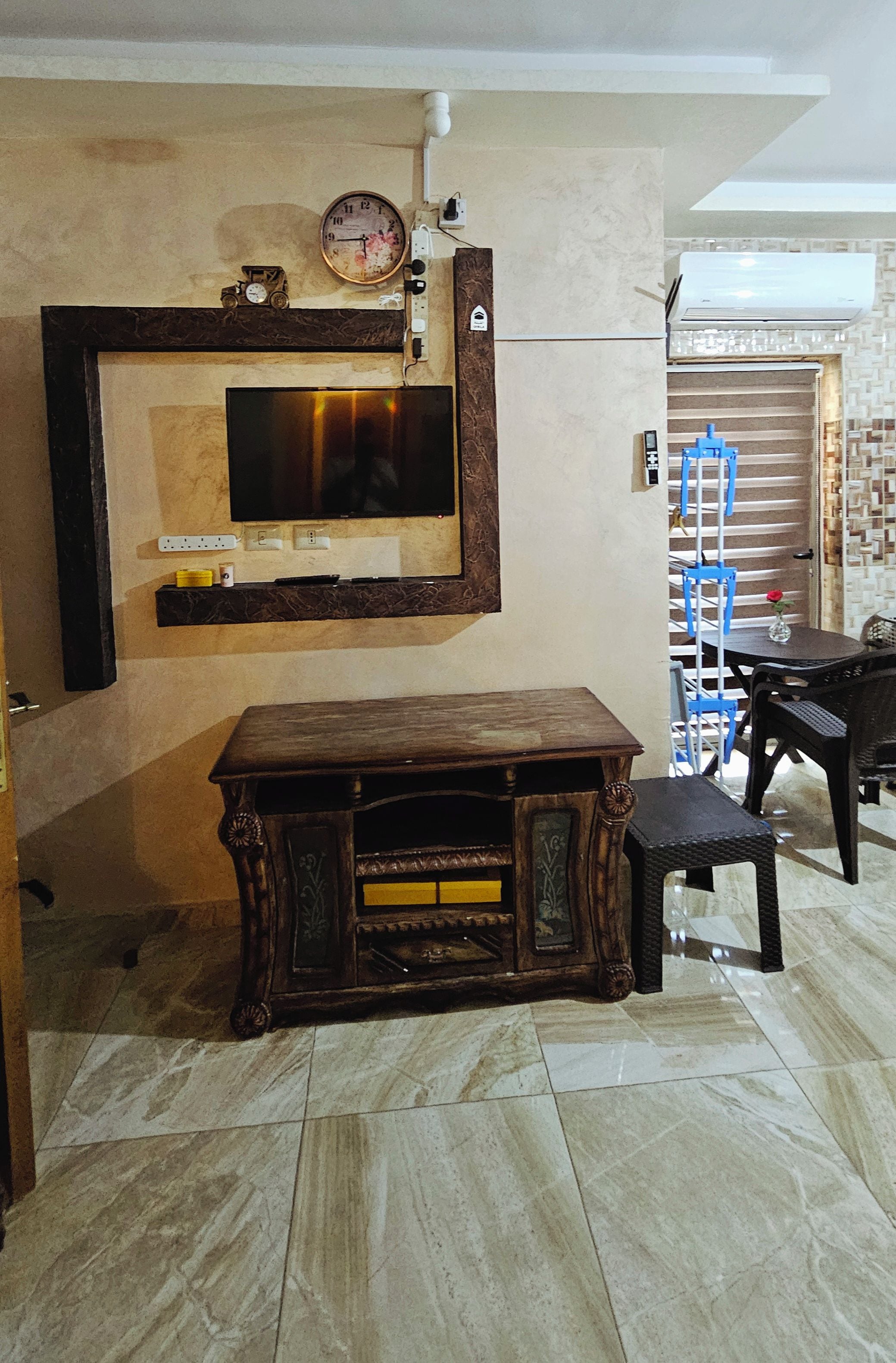 A room with a television mounted on the wall, a wooden cabinet, a bench, and a staircase leading to an upper level.