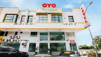 Ein Hotel namens 'OYO First Garden Hotel' mit modernem Design, das mehrere Klimaanlagen, einen einladenden Eingang und eine gut sichtbare Kontaktnummer zeigt.