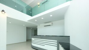 Un área de recepción moderna con un separador de vidrio, mostrador de recepción y unidad de aire acondicionado suspendida del techo.