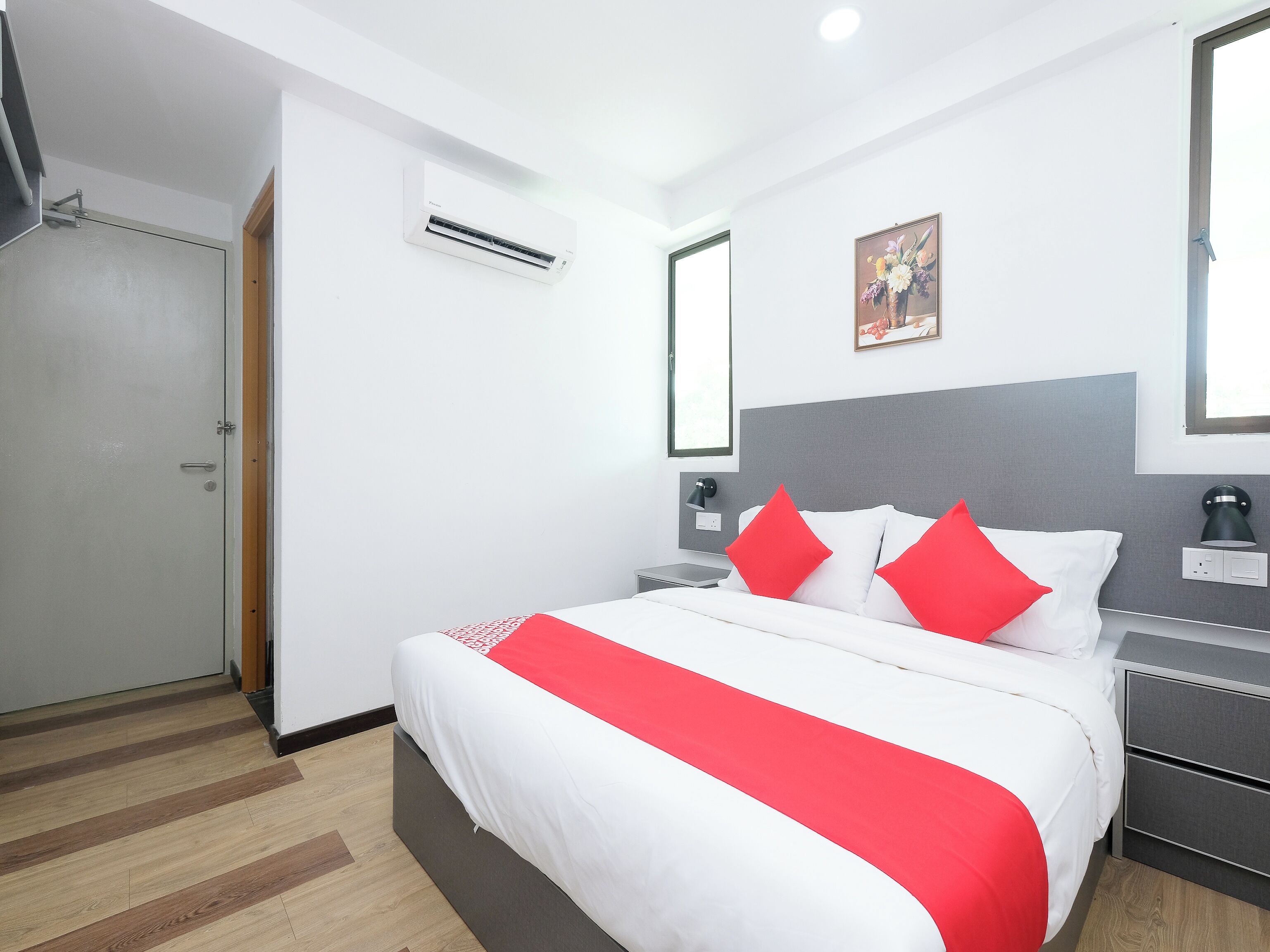 A modern hotel room with a large bed, a bedside table, a nightstand, a wall-mounted air conditioner, and a door.