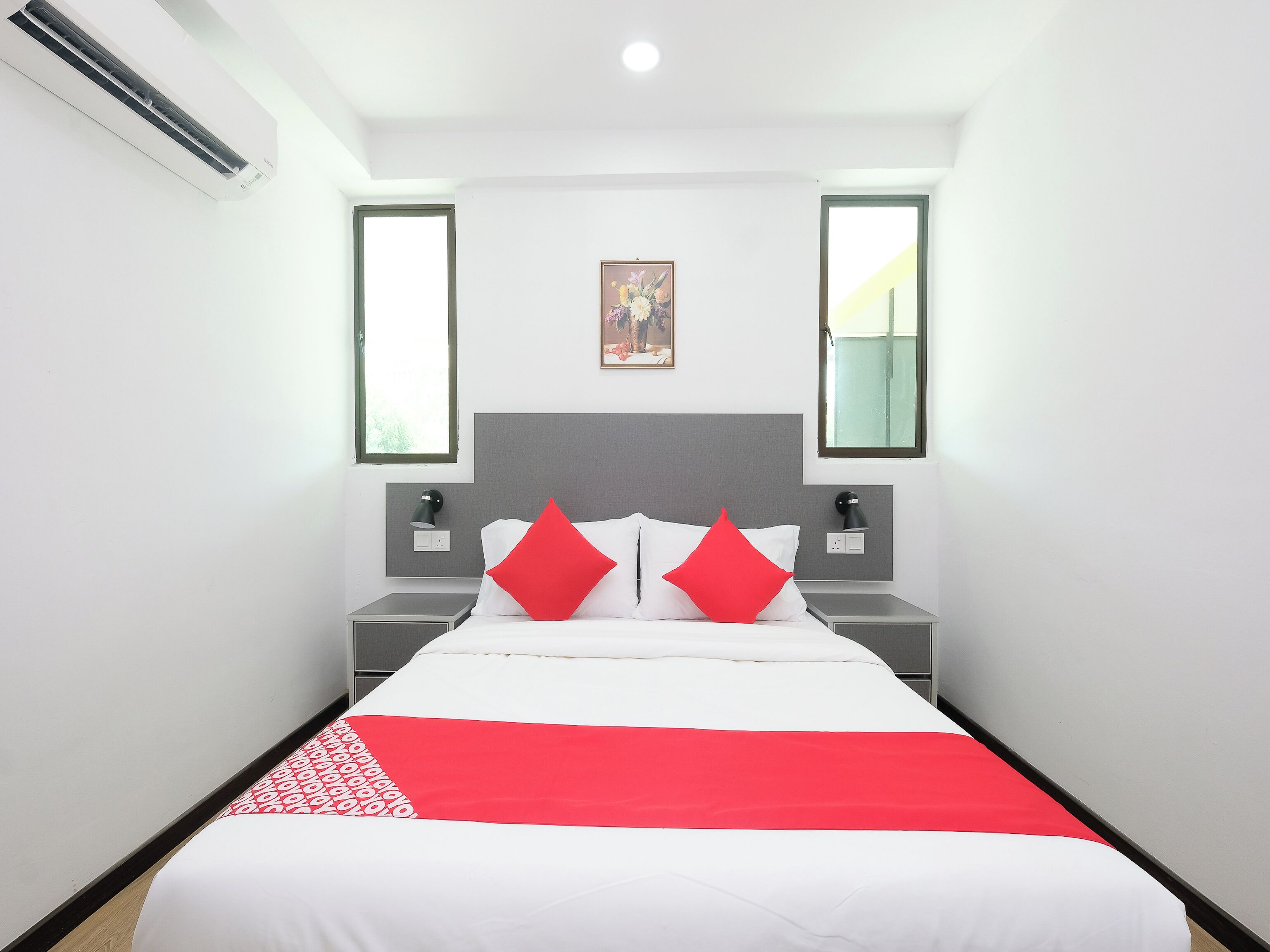 A hotel room with a bed, two bedside tables, a nightstand, a wall-mounted lamp, and a window.