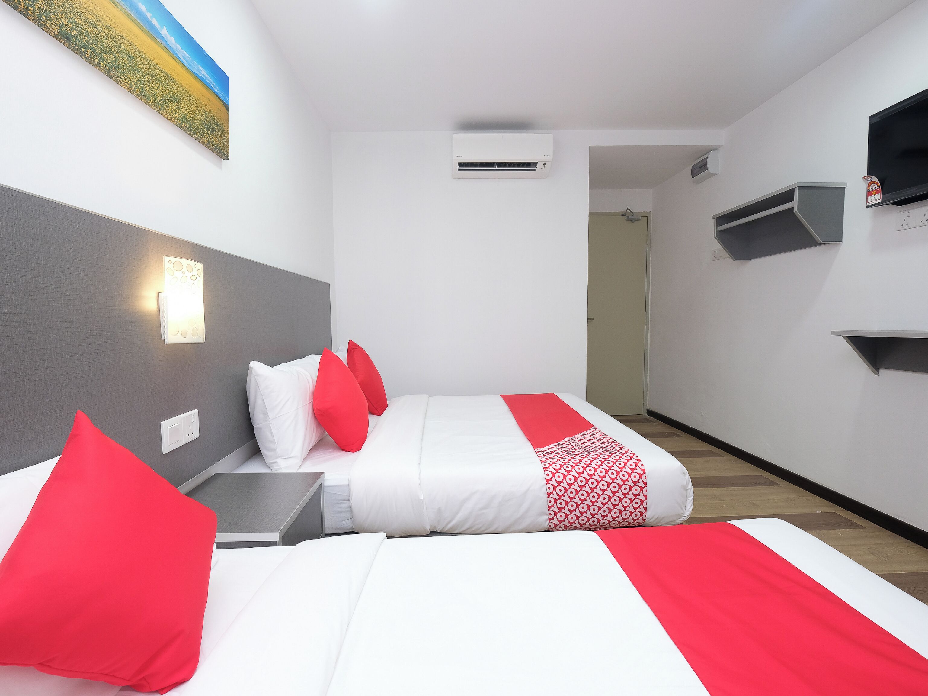 A hotel room with a bed, a nightstand, a red and white patterned blanket, and a painting on the wall.