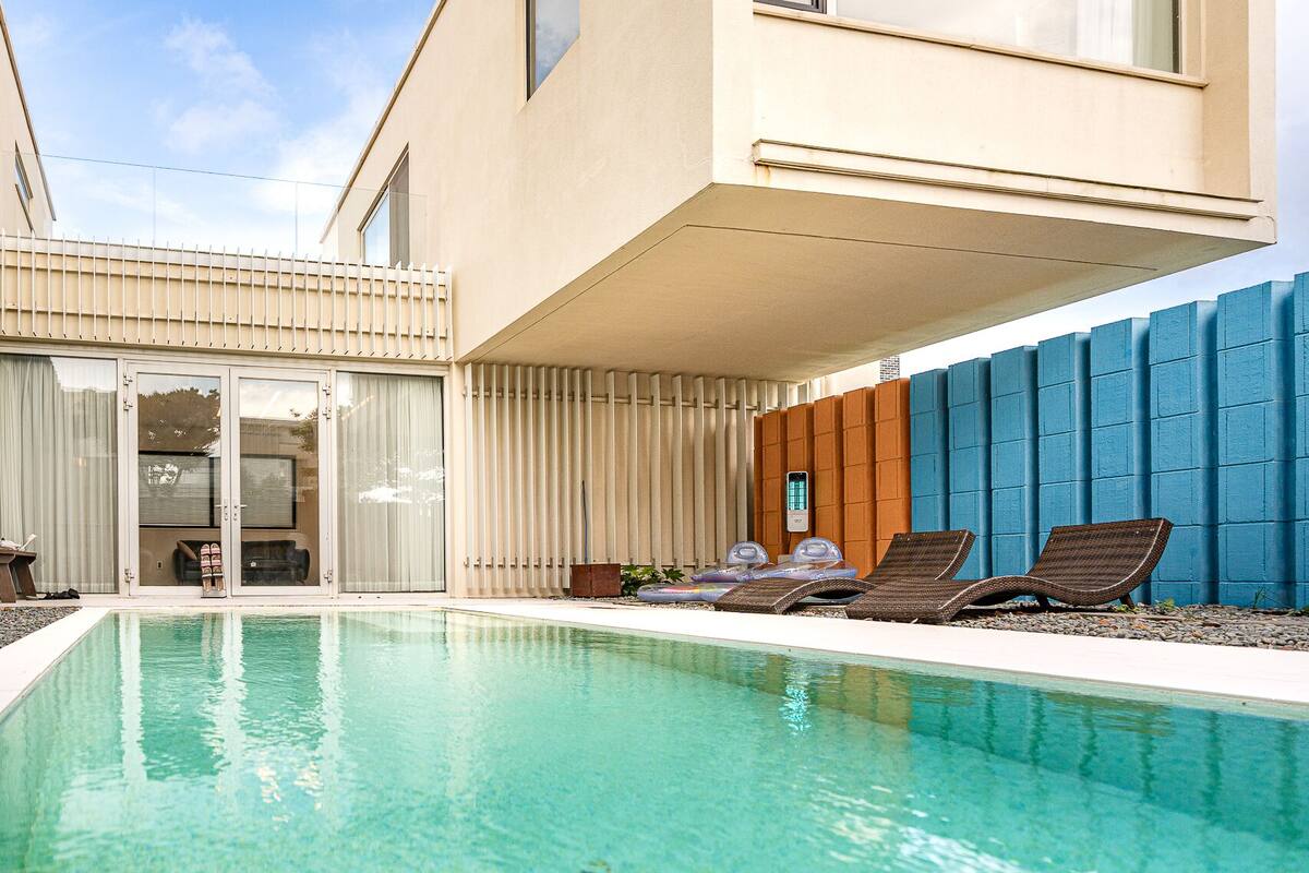Een modern huis met een zwembad, ligbedden en een overdekt terras.