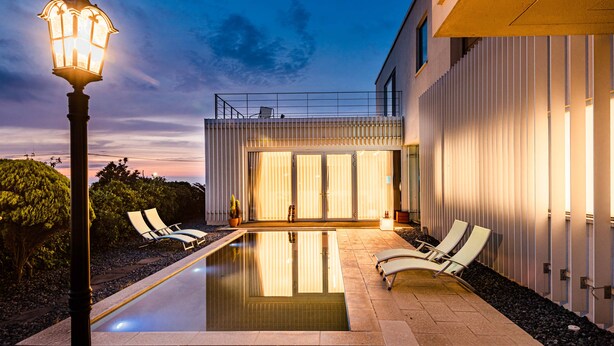 Una casa moderna con piscina, mobiliario de exterior y farola.