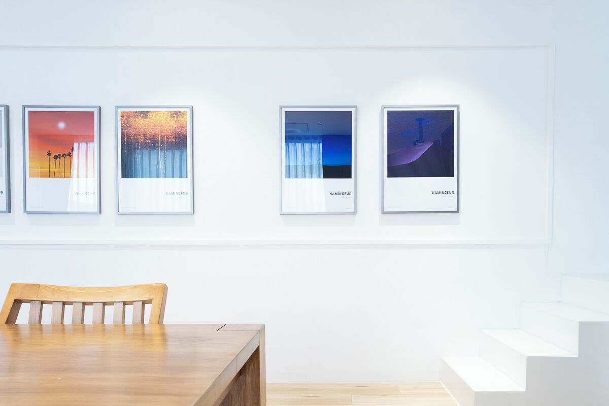 A gallery with framed artworks on the wall, a wooden table, and a staircase.
