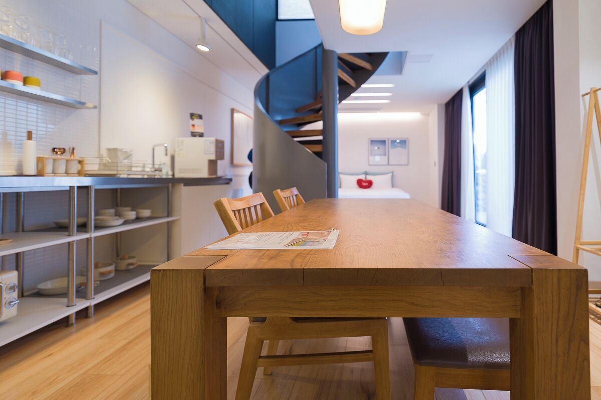 A modern kitchen with a wooden dining table, chairs, and a staircase leading to a loft area.