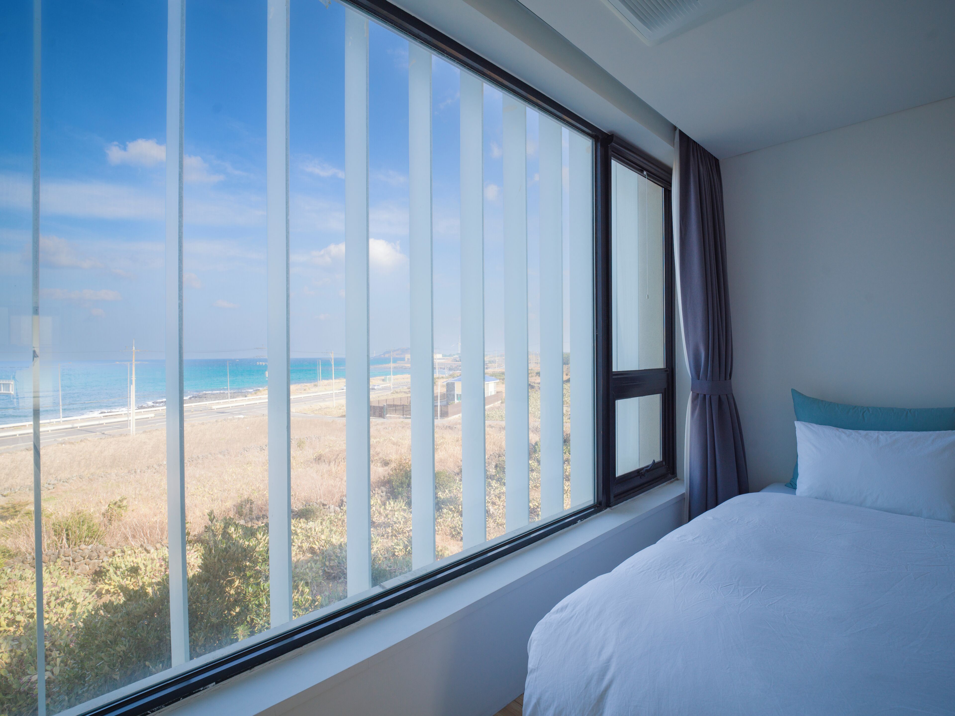 A bedroom with a large window overlooking a beach and road.