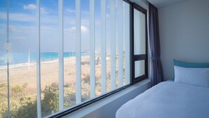 Un dormitorio con un amplio ventanal con vistas a una playa y una carretera.