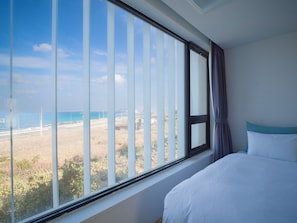 Quarto com uma grande janela com vista para uma praia e uma estrada.