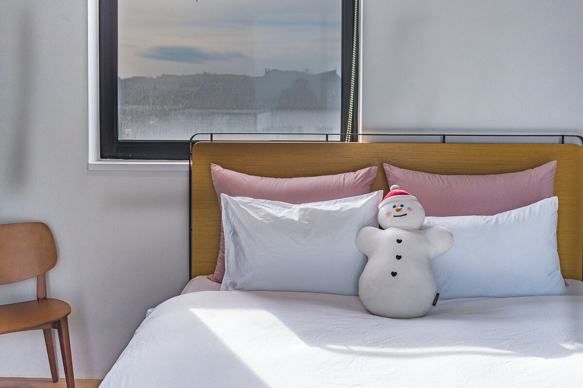 Cama com roupa de cama branca, cabeceira de madeira e um bicho de pelúcia de boneco de neve.