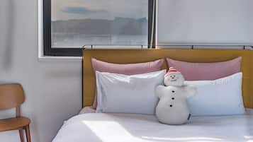 Cama com roupa de cama branca, cabeceira de madeira e um bicho de pelúcia de boneco de neve.