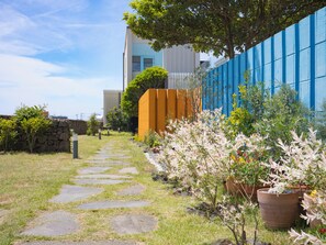 A garden pathway leading to a building with a blue wall and a stone wall on one side. - Namib Pool Villa Jeju (Jeju City)