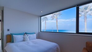 Un dormitorio con un amplio ventanal que ofrece vistas a palmeras y al océano.