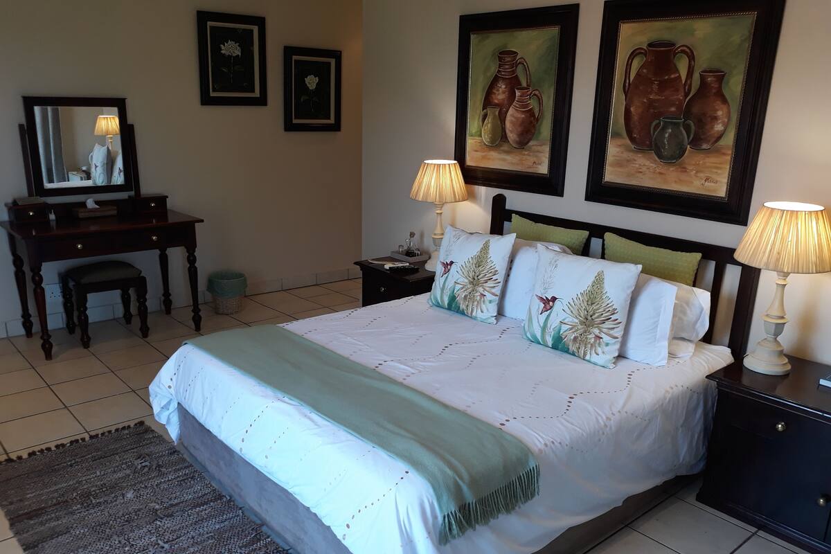 A neatly arranged bedroom with a bed, bedside tables, a desk, and a chair.