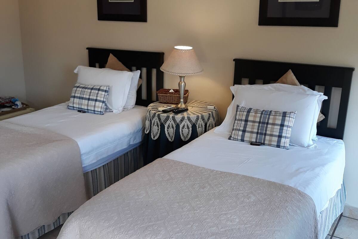 A hotel room with two single beds, a nightstand with a lamp, and two framed pictures on the wall.
