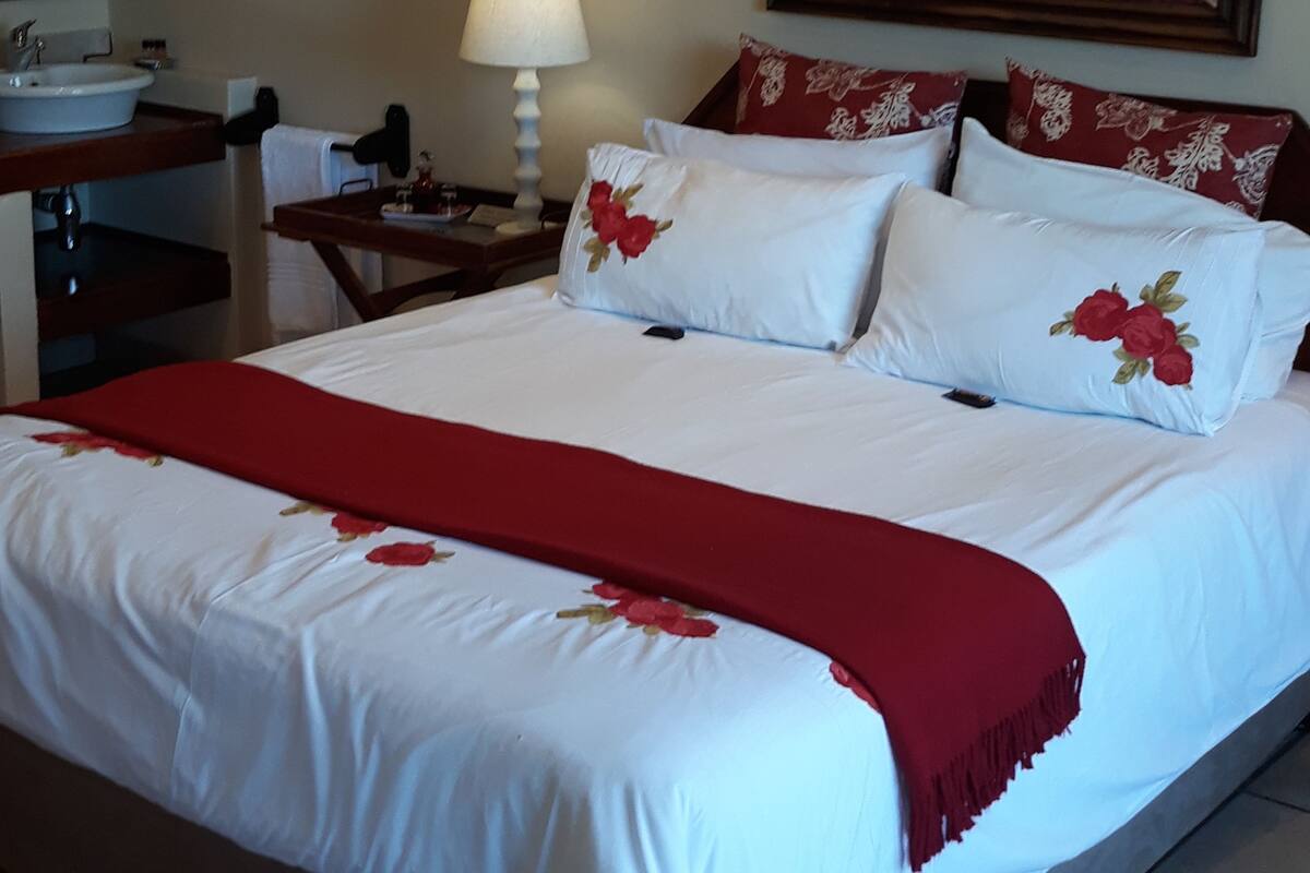 A hotel room with a large bed, a bedside table with a lamp, a painting on the wall, and a bathroom with a sink and mirror.