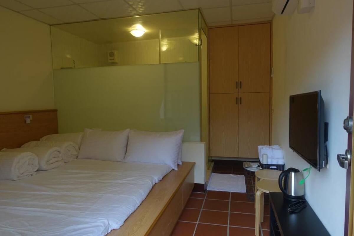 Una habitación de hotel con una cama, un armario de madera, una mesita con una tetera y un televisor en la pared.