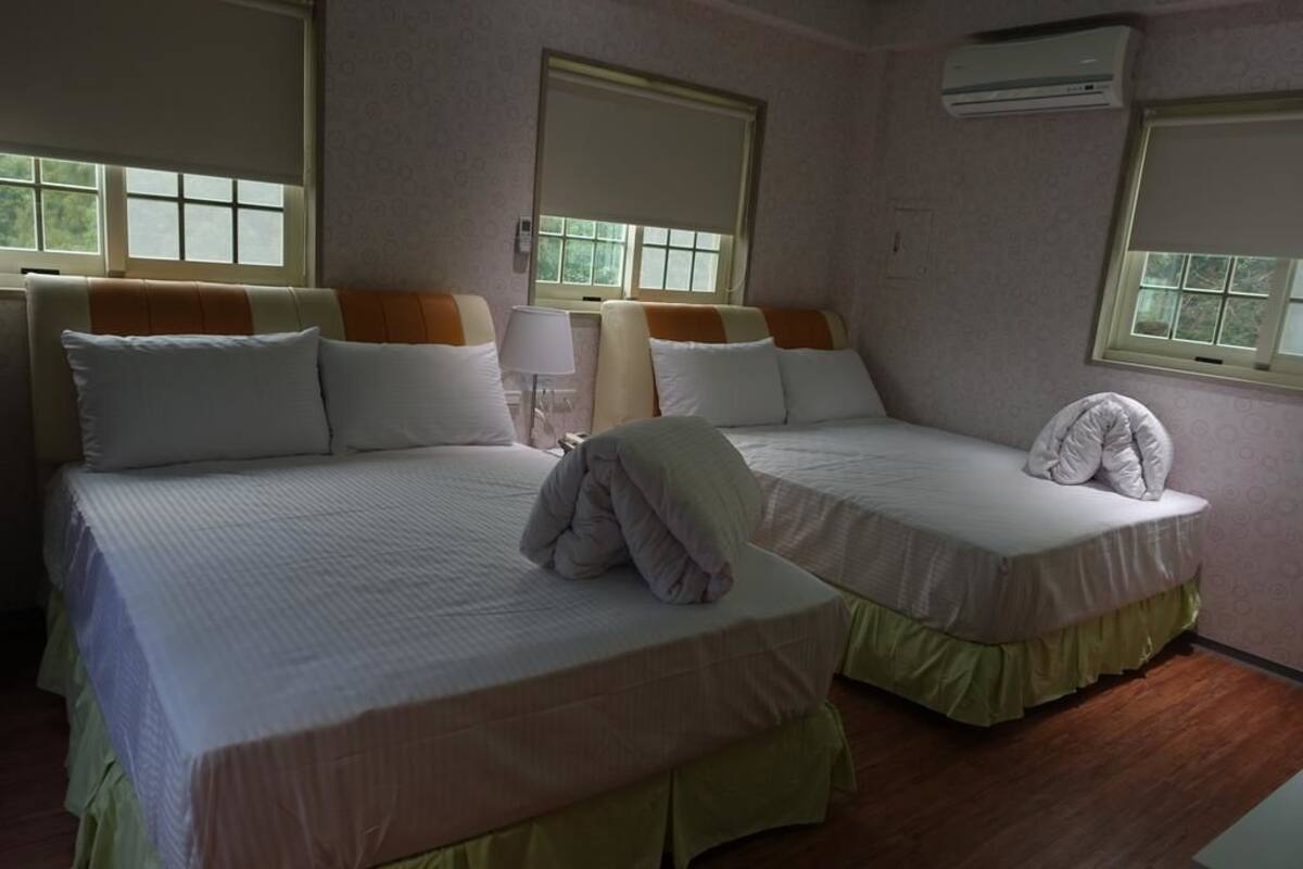 Habitación de hotel con dos camas, una ventana, aire acondicionado y una lámpara.