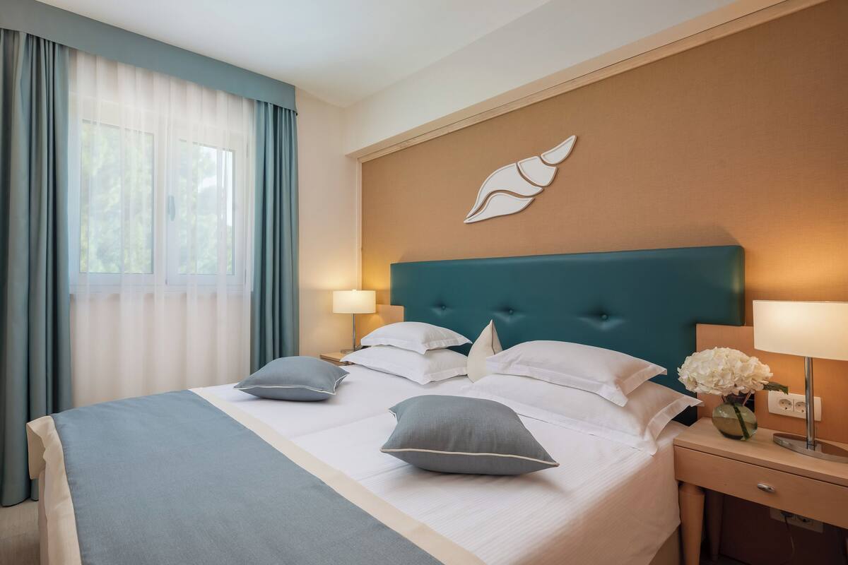 A neatly made bed with pillows, a bedside lamp, and a vase with flowers on a nightstand.