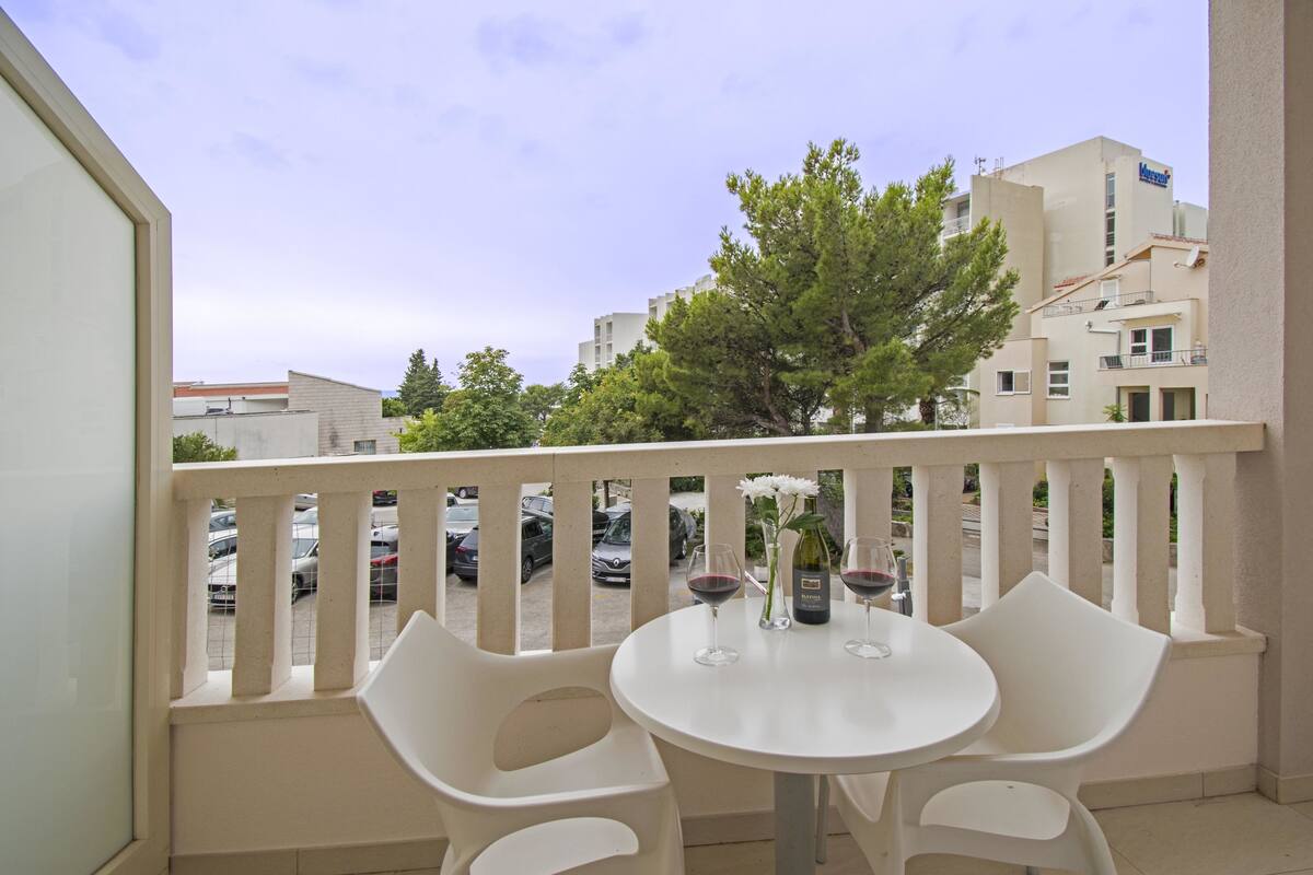 A balcony with a white table and chairs, two wine glasses, and a bottle of wine.