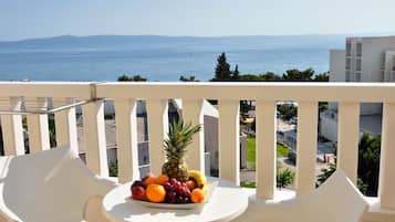Ein Balkon mit Tisch, gedeckt mit Obst, mit Blick auf die Küste, Gebäude und einen klaren Himmel.