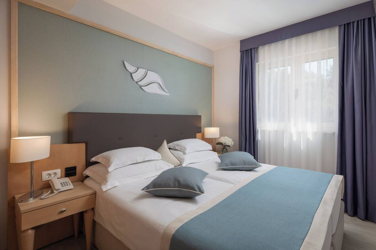 A hotel room with a bed, nightstand, lamp, and a wall-mounted phone.