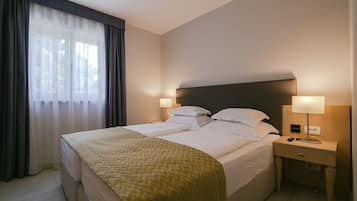 Ein Hotelzimmer mit einem Doppelbett, zwei Nachttischen, einer Lampe und einem Fenster mit Vorhängen.