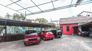 A covered parking area with several cars parked, a red building, and a metal roof structure.