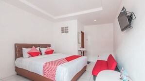 A hotel room with a bed, a bedside table, a chair, a TV mounted on the wall, and a water bottle on the table.