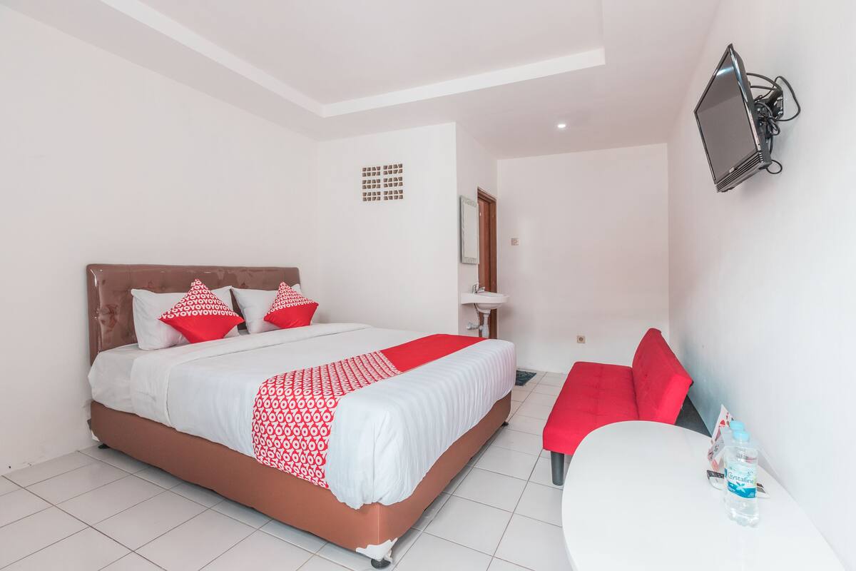 A hotel room with a bed, a bedside table, a chair, a TV mounted on the wall, and a water bottle on the table.