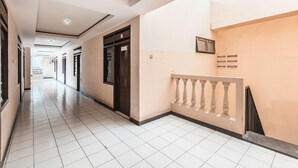 A corridor with tiled flooring, a staircase with a balustrade, and a door with a sign.