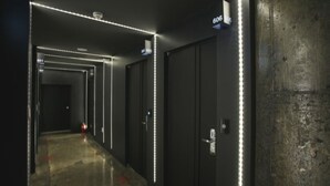 A hallway with dark walls, illuminated by linear LED lights along the ceiling and walls. There are doors with numbers above them, indicating room numbers. - Hotel Yaja Suwon City Hall (Suwon)