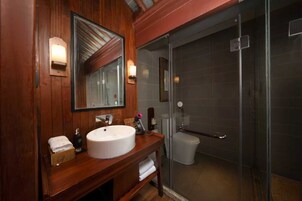 Un baño con tocador de madera, un espejo grande, un lavamanos blanco y una ducha con cerramiento de vidrio.
