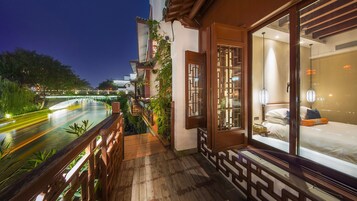 Un balcón con vista al río, piso de madera y una ventana de estilo tradicional con celosía decorativa.