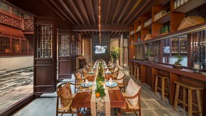 A traditional Chinese restaurant with a long wooden dining table set for a meal, surrounded by wooden chairs and a bar area with shelves. - SSAW Boutique Hotel Nanjing Qifeng Confucius House (Nanjing)
