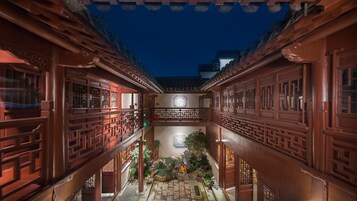 Un patio tradicional con arquitectura de madera, un jardín central y un cielo nocturno.