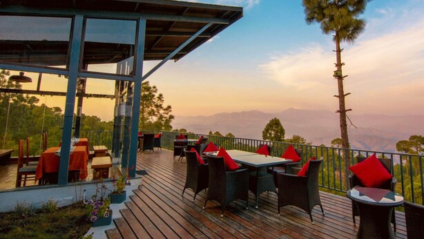 An outdoor dining area with tables and chairs, overlooking a mountainous landscape. - Queens Meadows by Sunshine & Smiles (Ranikhet)