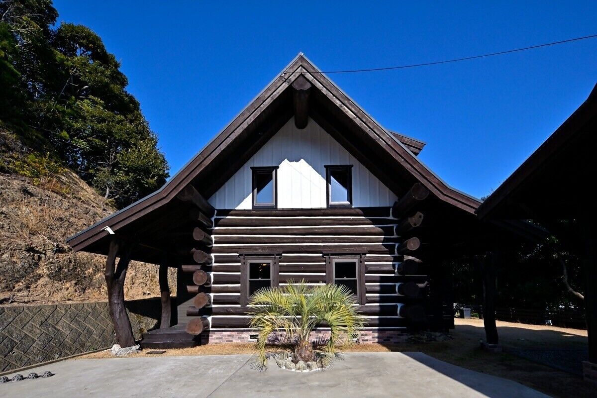 A log cabin with a triangular roof, a central chimney, and a small porch area.