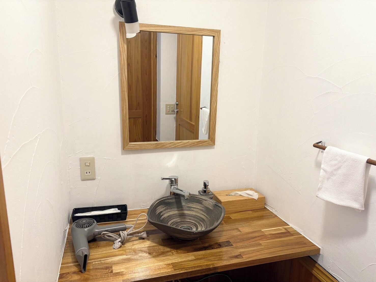 Une salle de bain avec un meuble-lavabo en bois, un lavabo en verre, un miroir, un porte-serviettes et un sèche-cheveux posés sur le comptoir.