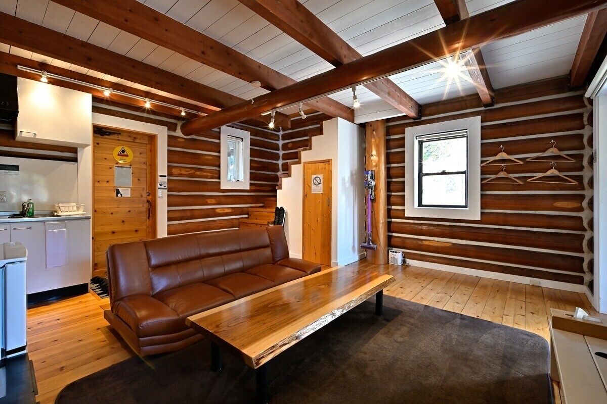 Interno di una baita di legno con una panca in legno, un divano in pelle e un angolo cottura.