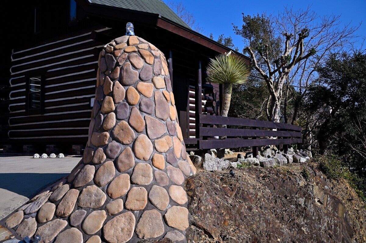 A stone structure with a chimney, a wooden fence, and a building in the background.