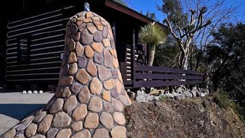 A stone structure with a chimney, a wooden fence, and a building in the background.