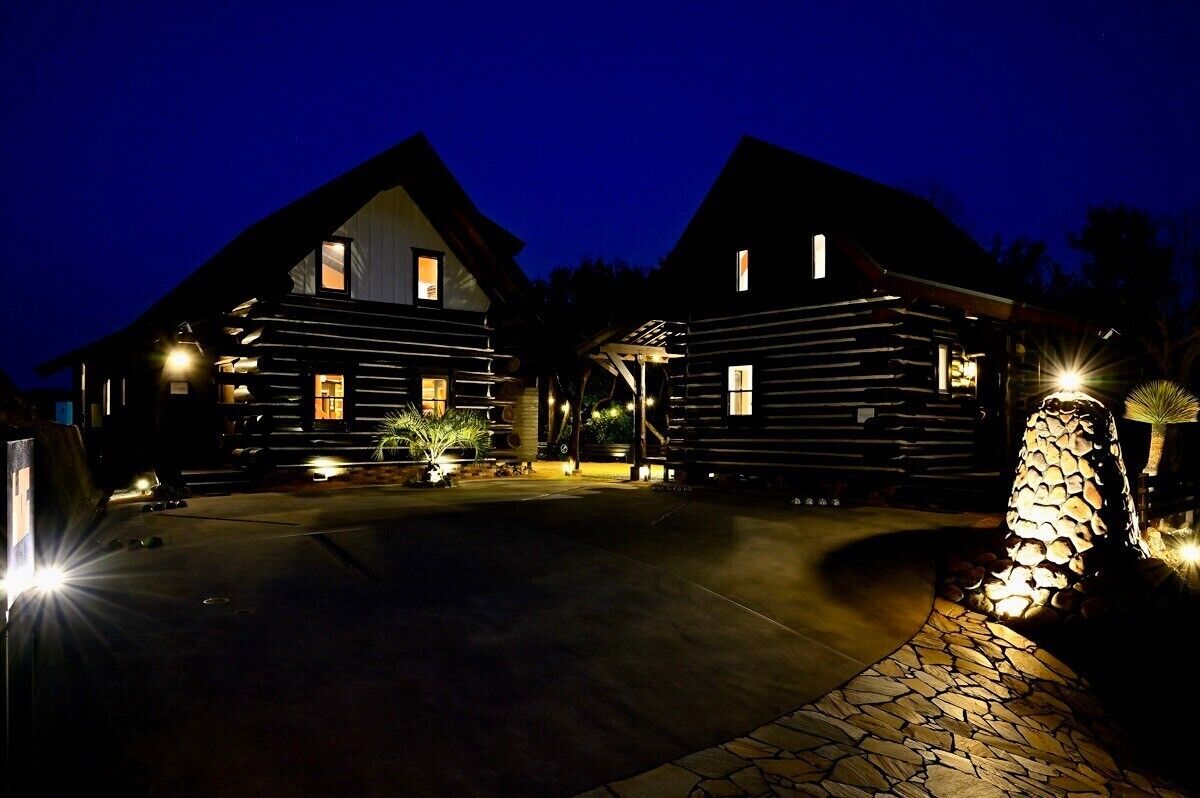 Una baita di legno con un vialetto in pietra che conduce all'ingresso, circondata da una strada d'accesso ben illuminata e una struttura decorativa in pietra.