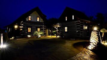 Una baita di legno con un vialetto in pietra che conduce all'ingresso, circondata da una strada d'accesso ben illuminata e una struttura decorativa in pietra.