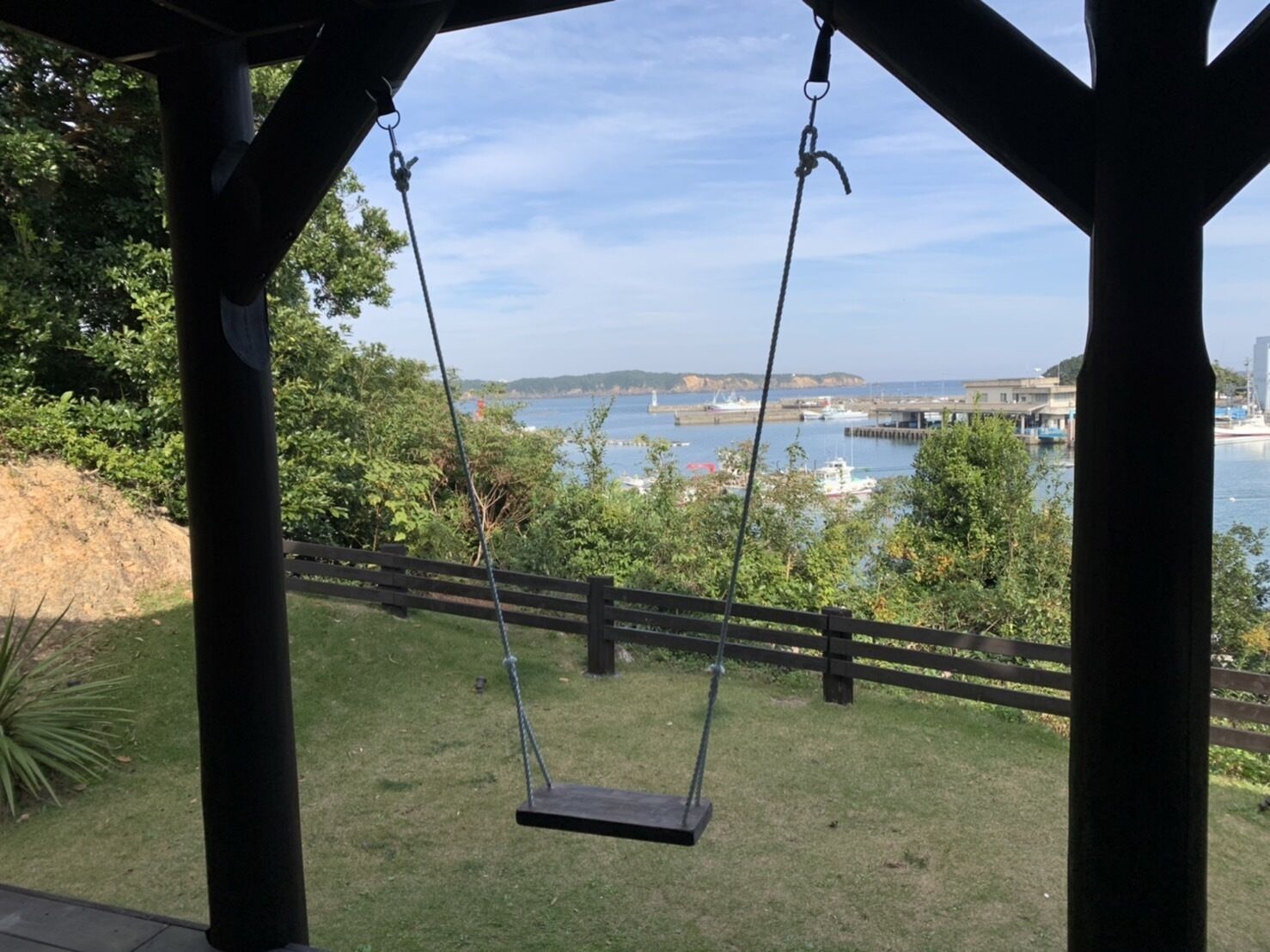 A wooden swing set overlooking a body of water with boats and a distant shoreline.