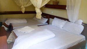 Une chambre avec deux lits, chacun doté de draps et d’oreillers blancs, d’une tête de lit en bois et d’une moustiquaire au-dessus d’un des lits.