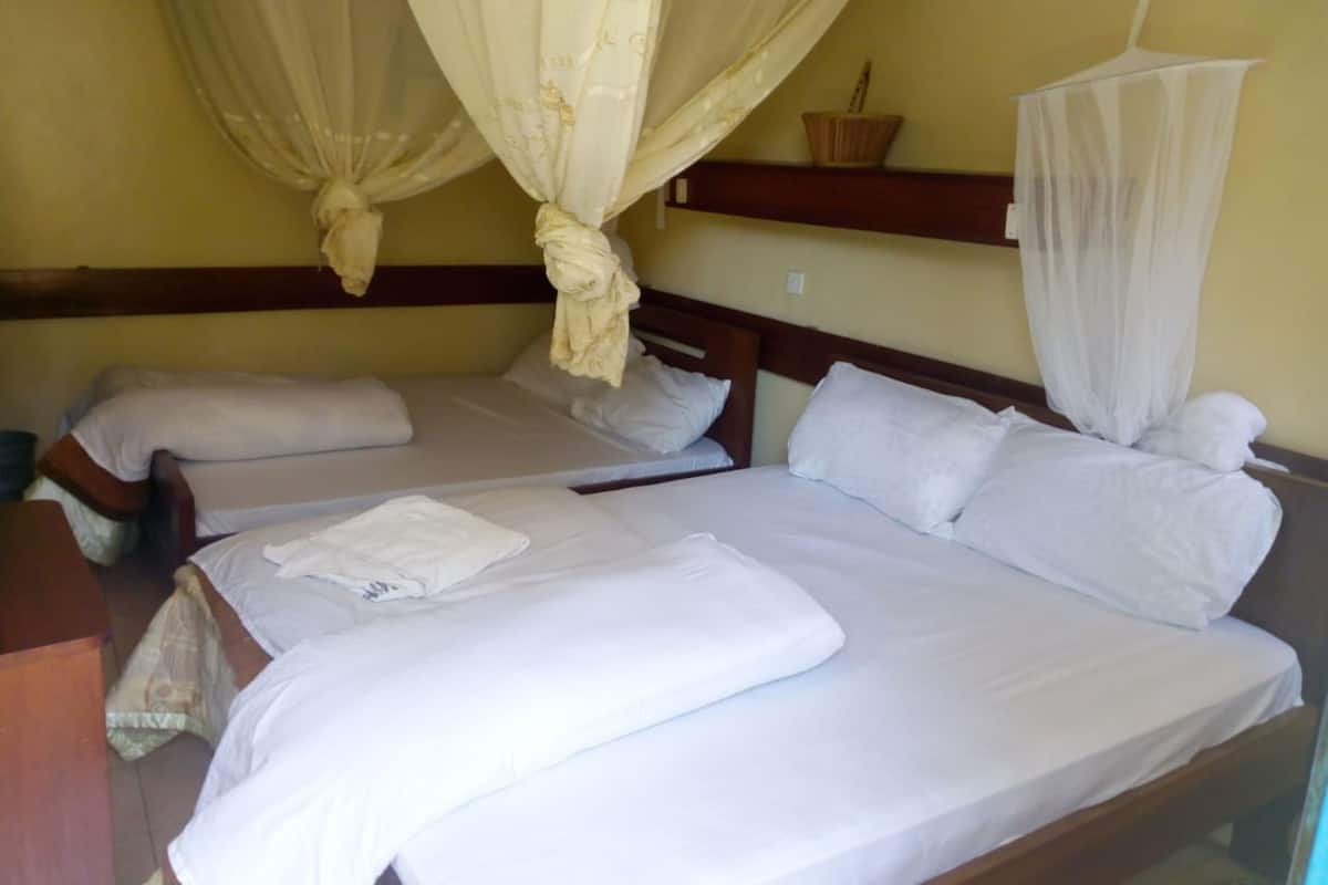 Ein Zimmer mit zwei Betten, jeweils mit weißer Bettwäsche und Kissen, einem Holzkopfstück und einem Moskitonetz über einem Bett.
