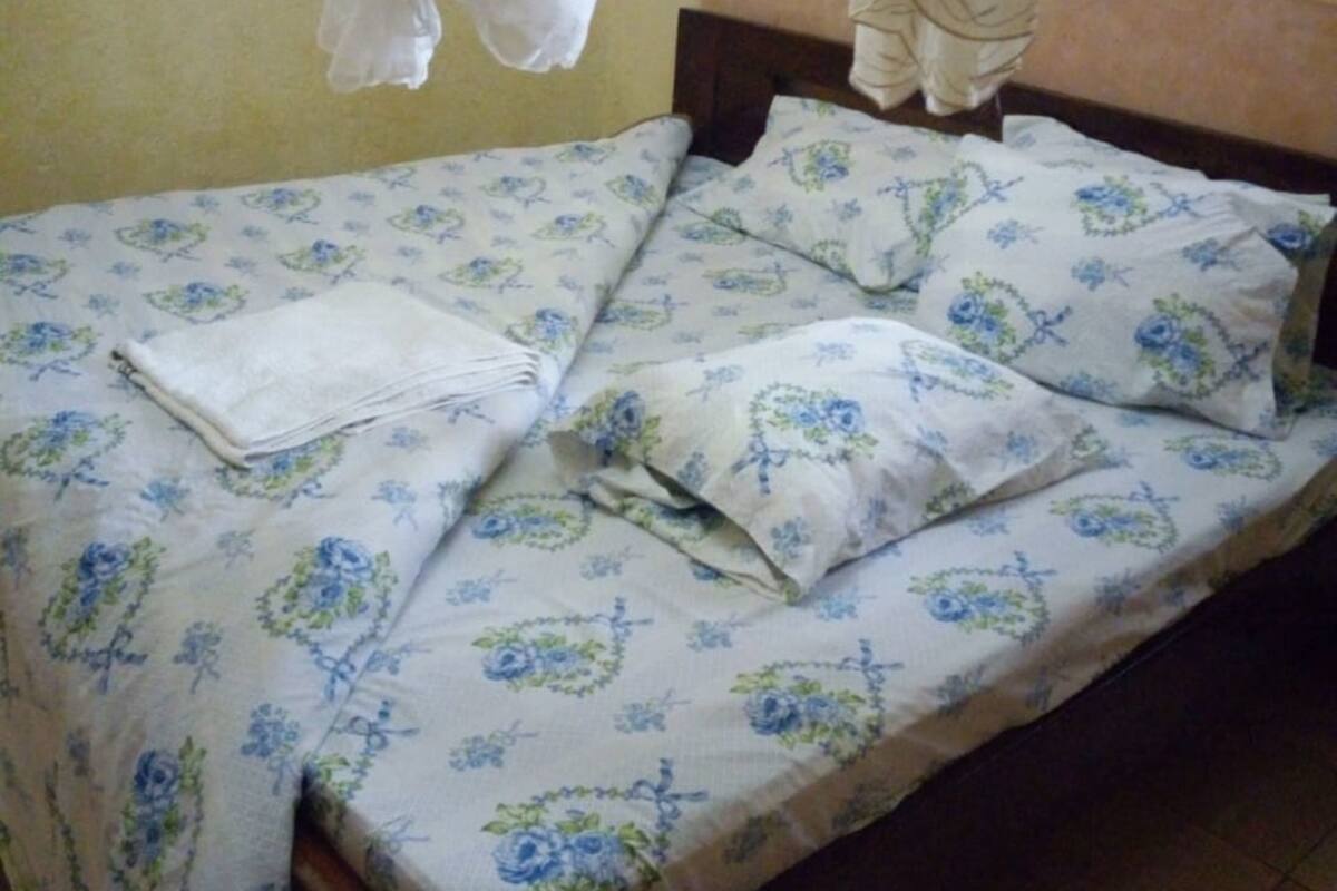 Ein Einzelbett mit floraler Bettwäsche, einem Holz-Kopfschild und einem Moskitonetz.
